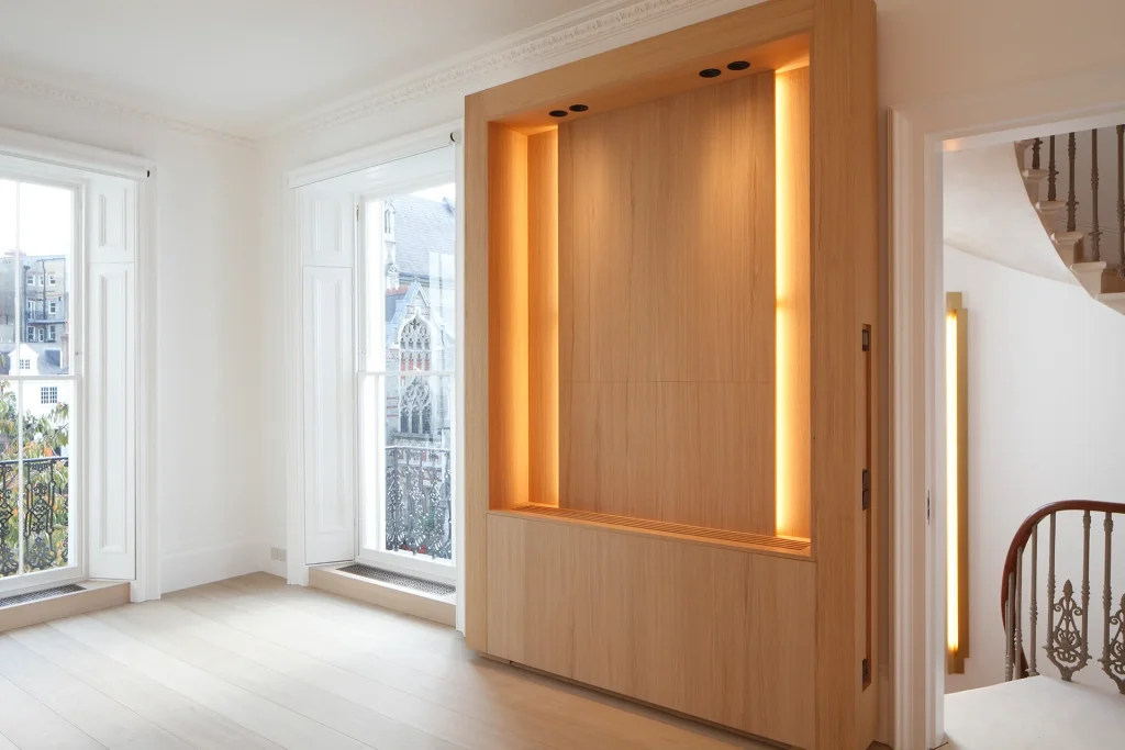This room showcases exquisite architecture with its wooden flooring and a built-in lighted wooden cabinet. Large windows with shutters invite natural light, while a stylish spiral staircase adds to the design's elegance. Map Projects