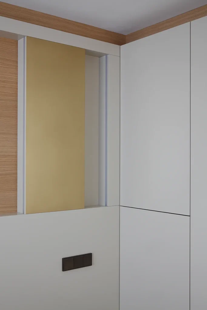 A modern interior corner showcases a seamless blend of design and architecture, featuring white and light wood cabinets accented by a gold panel and a dark electrical switch. Map Projects