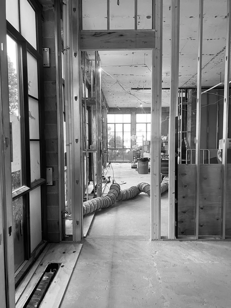 Black and white photo of a building under construction, showcasing striking architecture with exposed wooden framing, large windows, and a coiled ventilation hose on the floor. Map Projects