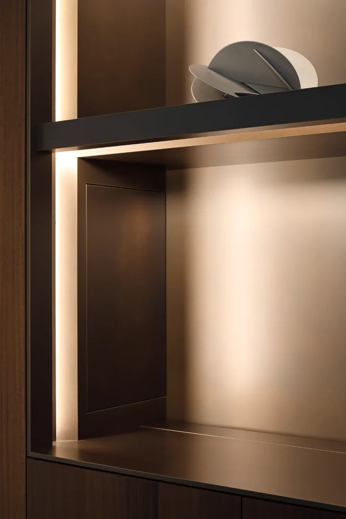 A dark wooden shelf with built-in lighting showcases a round, abstract gray sculpture on the top shelf, seamlessly blending modern design and architecture. Map Projects
