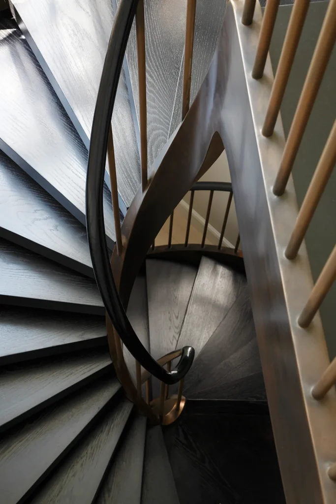 A stunning example of architectural design, this spiral staircase features dark wooden steps and gold-colored vertical railings, elegantly descending in a circular pattern. Map Projects