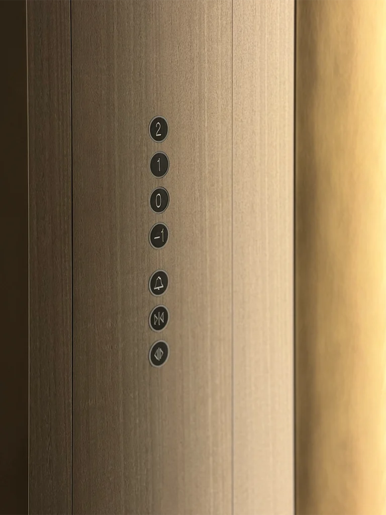 Vertical bronze lift call button panel integrated into the wall with minimal detailing