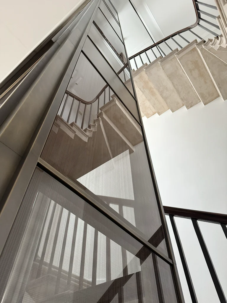 Completed lift shaft viewed through existing stair void, with glass reflections and bronze framing