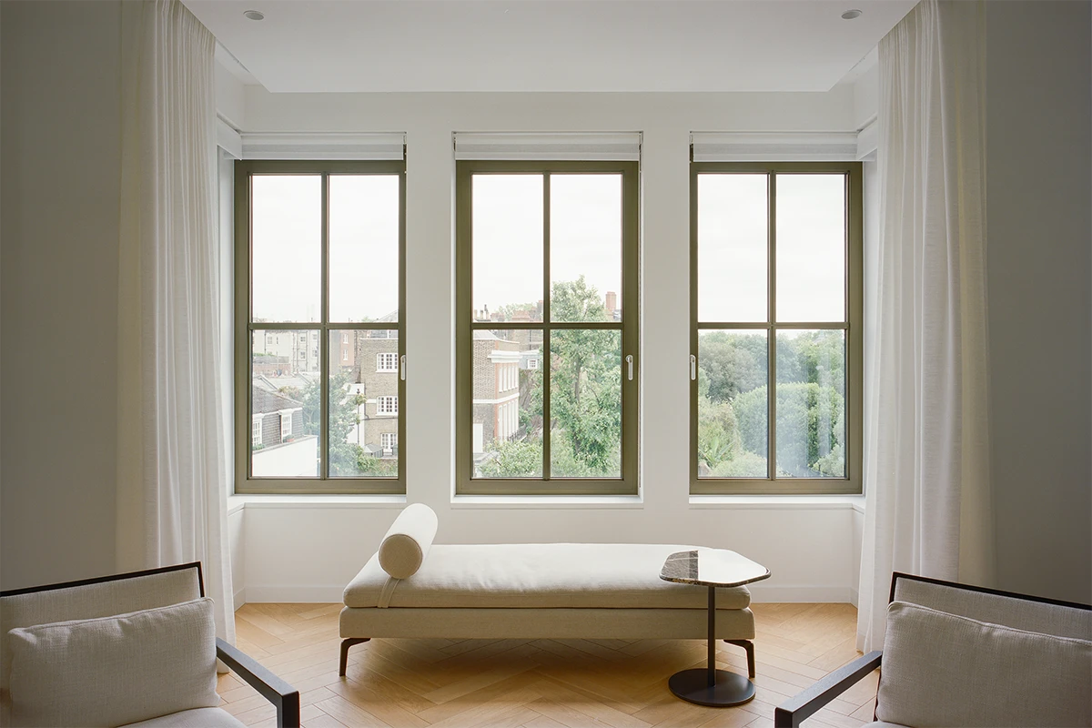 Interior of a minimalist living room with floor-to-ceiling windows overlooking treetops and city buildings