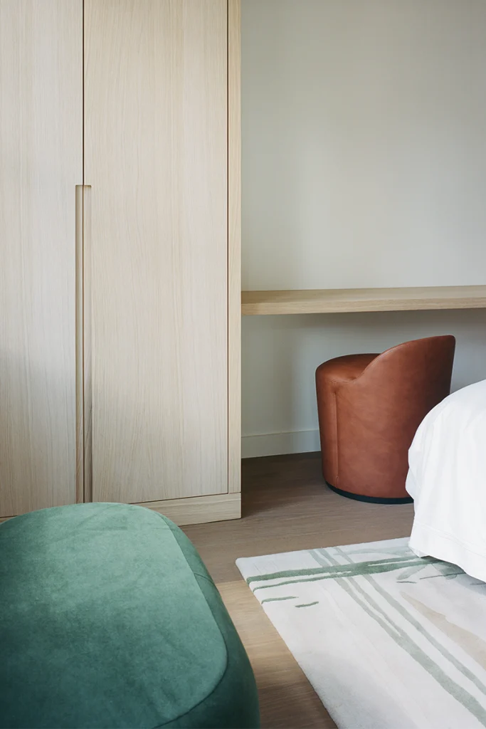 Bedroom with light oak wardrobe, green ottoman, leather chair and integrated desk nook