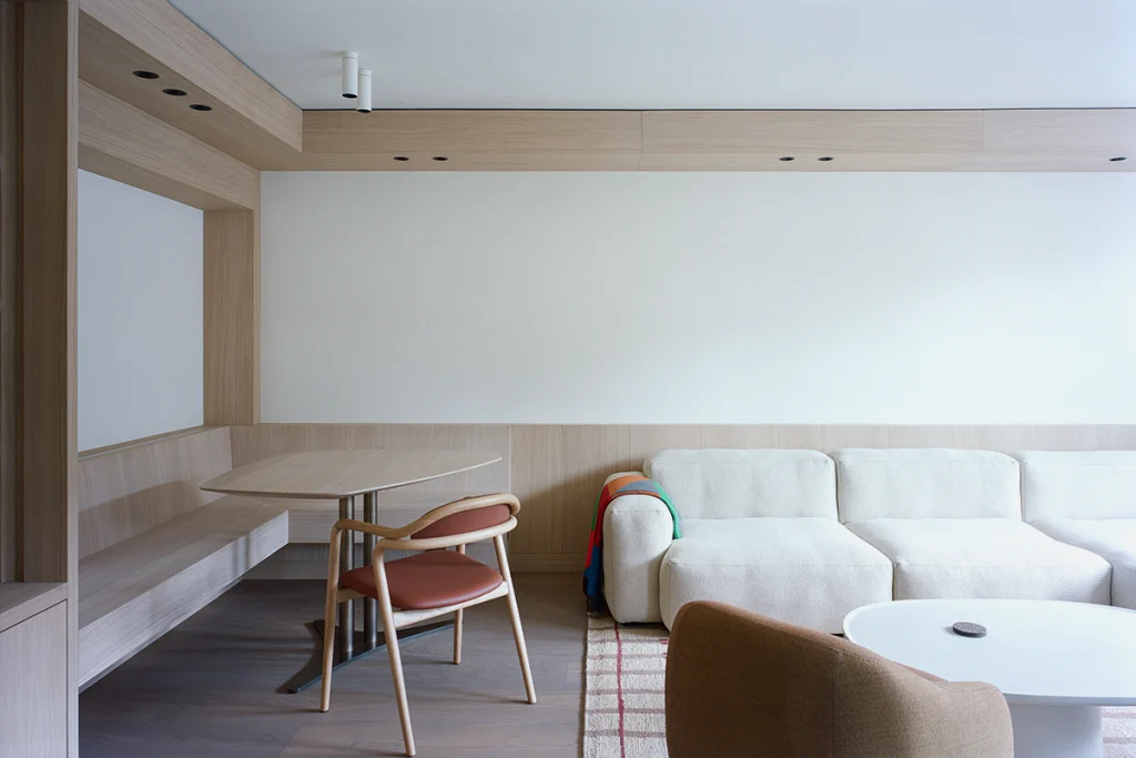 Full living room setup with L-shaped sofa, oak shelving, white walls and curated furniture creating a calm, layered interior