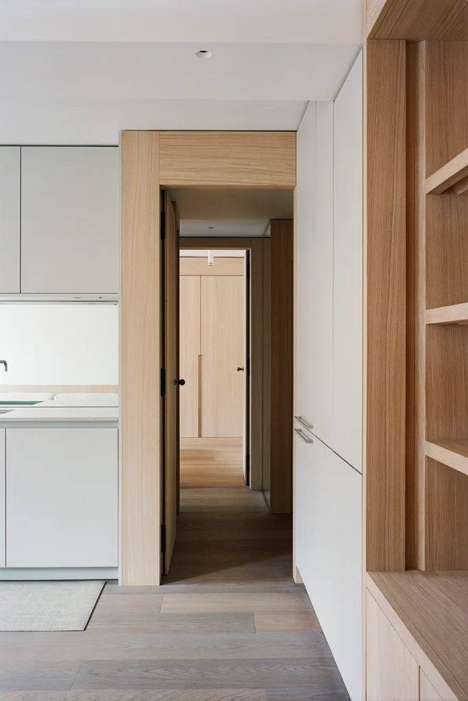 Corridor view showing compact kitchen cabinetry and floor-to-ceiling oak shelving
